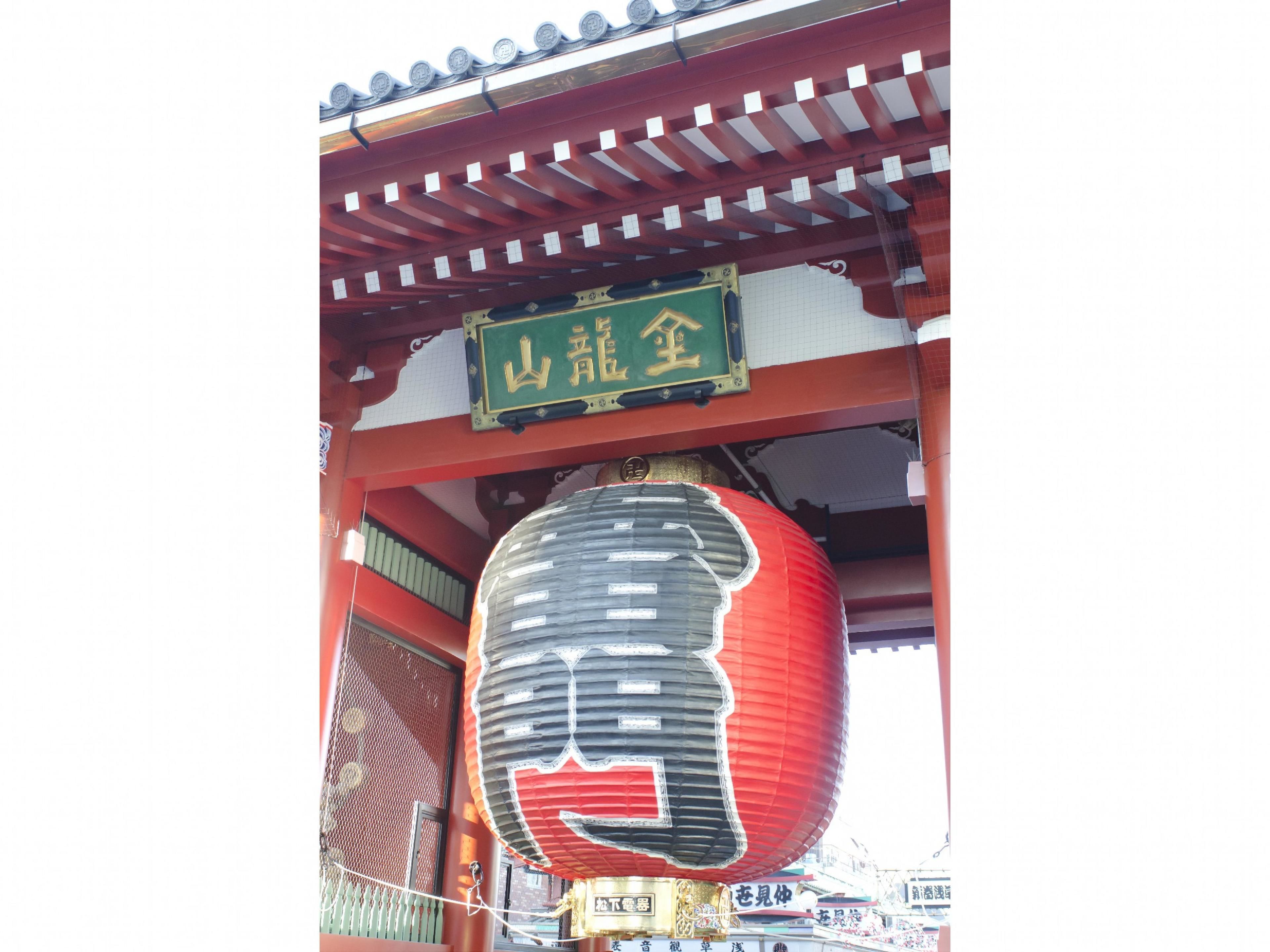 Une porte traditionnelle japonaise, sous laquelle est suspendue une lanterne rouge.