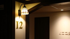 A hallway with a lit wall lamp, a number '12' sign, and a door. - KOKO HOTEL Ikebukuro (Tokyo)