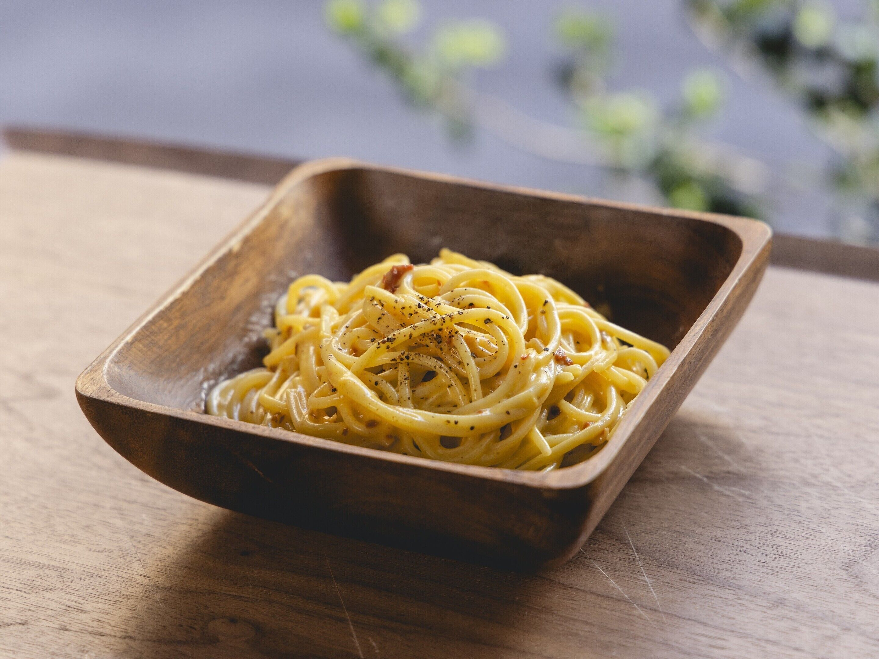 A wooden bowl containing spaghetti with a garnish, placed on a wooden surface.