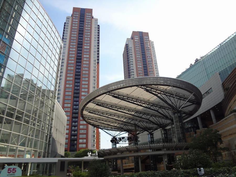 Una plaza urbana moderna con edificios altos, una estructura circular de vidrio distintiva y un cielo despejado.