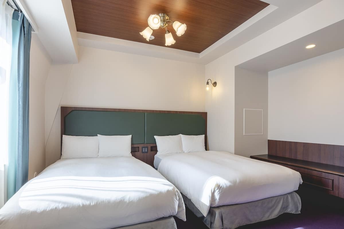 A hotel room with two beds, a wooden ceiling, and a ceiling fan.