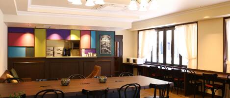 A restaurant with a long wooden table, black chairs, and a colorful wall with a menu board.