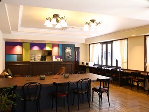 A restaurant with a long wooden table, black chairs, and a colorful wall with a menu board. - KOKO HOTEL Ikebukuro (Tokyo)