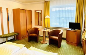 A hotel room with a bed, two armchairs, a small table, a TV, a wardrobe, a bench, and a window with curtains. - Hotel Ingeburg (Bad Sachsa)