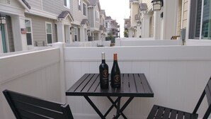 En balkon med to sorte metalstole og et bord, to flasker vin og udsigt til række af byhuse.