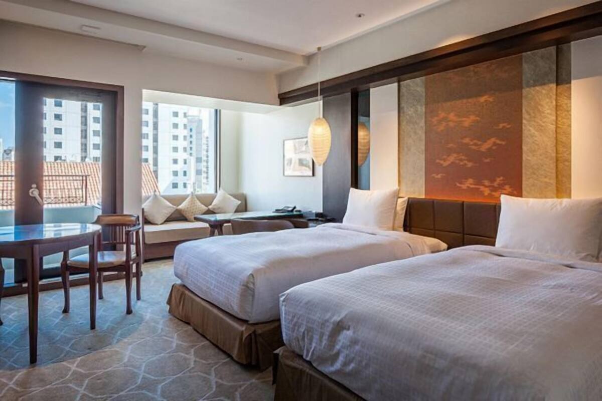 Een hotelkamer met twee bedden, een eettafel, een bank en uitzicht op gebouwen.