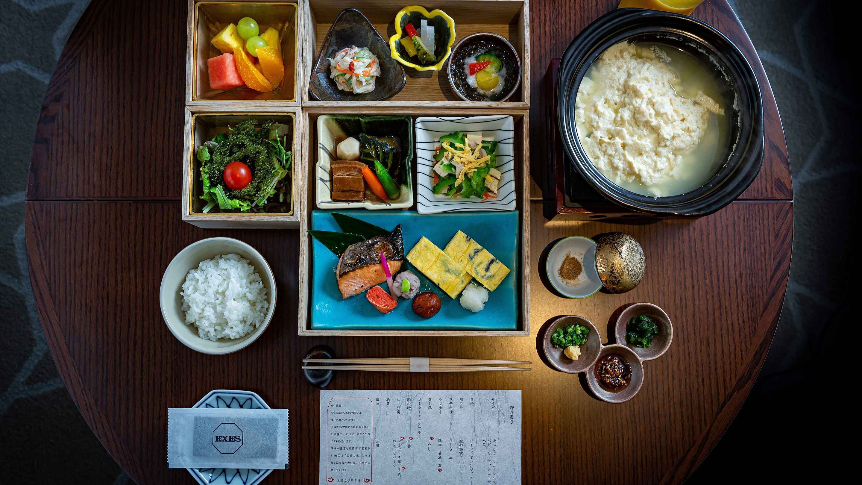 Una comida tradicional japonesa con diversos platos, incluyendo arroz, pescado y verduras, servida sobre una mesa de madera.