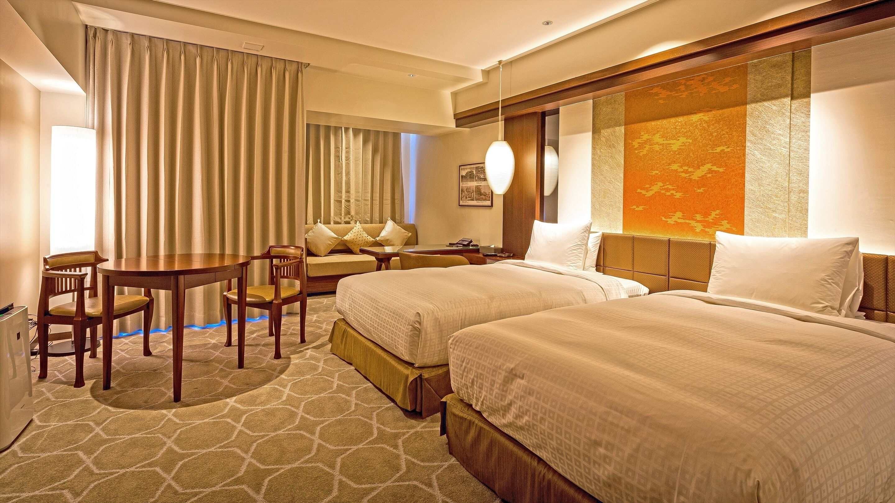 A hotel room with two beds, a desk, a chair, and a sofa.