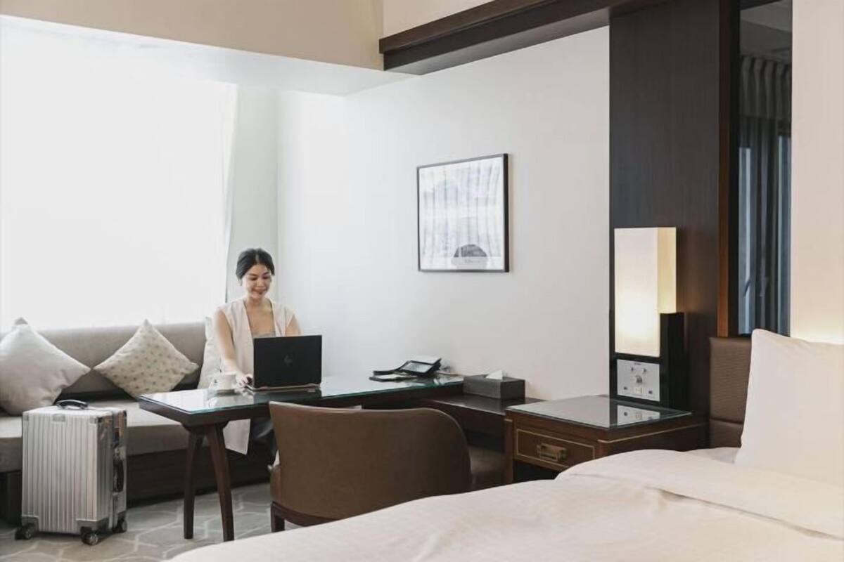 Hotelkamer met een bed, bureau met laptop, koffer, radiator en een lijst aan de muur.