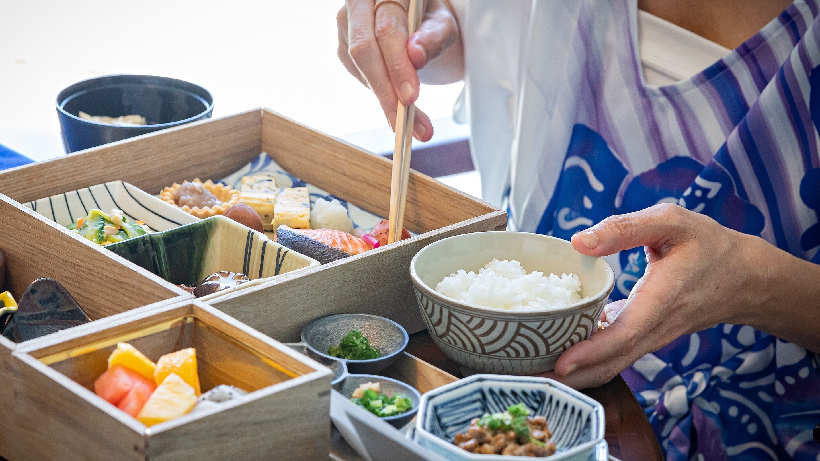 Una persona sirviendo sushi desde una bandeja de madera con varios compartimentos.