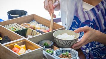 Una persona sirviendo sushi desde una bandeja de madera con varios compartimentos.