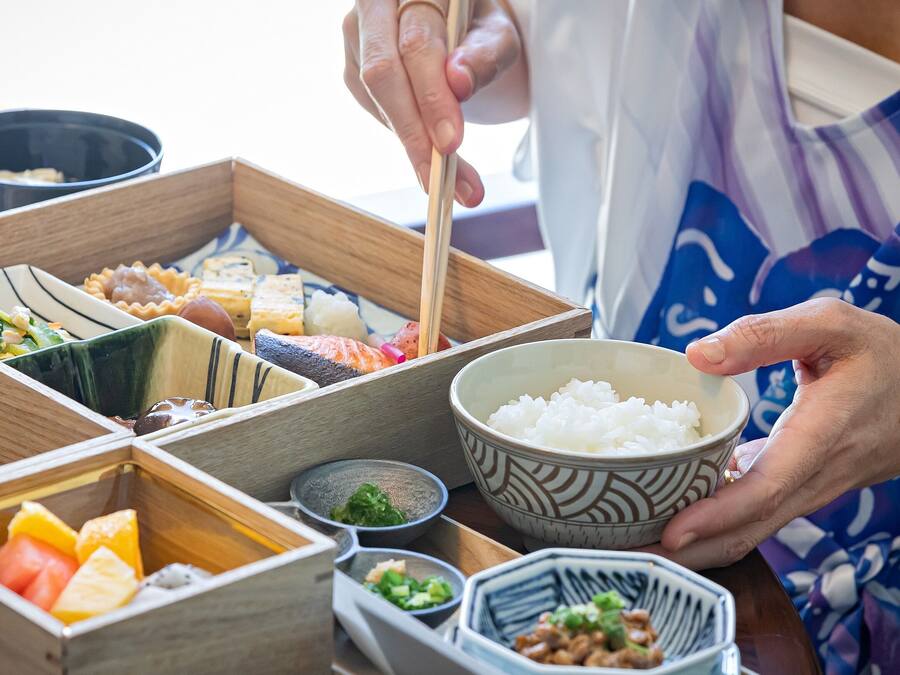 Una persona sirviendo sushi desde una bandeja de madera con varios compartimentos.