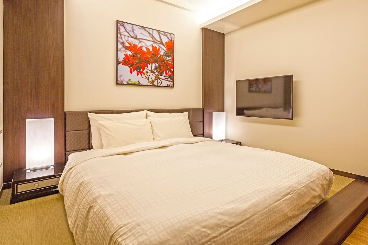 Een hotelkamer met een groot bed, een nachtkastje, een wandtelevisie en twee ingelijste foto's.