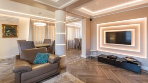 A modern living room with a leather sofa, a flat-screen TV mounted on the wall, a dining area with a table and chairs, and a large pillar with integrated lighting. - Villa Ciconia (Veliko Tarnovo)