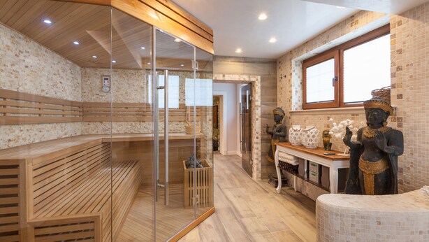 A spa room with wooden benches, a glass-enclosed sauna, a statue, and a window with a view. - Villa Ciconia (Veliko Tarnovo)
