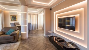 A modern living room with a large flat-screen TV mounted on the wall, a leather sofa, a coffee table, and a herringbone wood floor. - Villa Ciconia (Veliko Tarnovo)