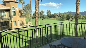 Een balkon met een tafel en stoelen, met uitzicht op een verzorgd gazon en een golfbaan.