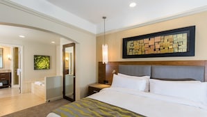Hotelkamer met een groot bed, een nachtkastje, een kunstwerk aan de muur en een badkamer zichtbaar door een geopende deur.