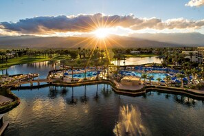 Ein Resort mit großem Pool, Palmen und einem Golfplatz im Hintergrund.