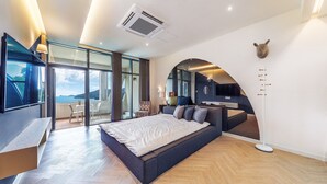 A modern bedroom with a large bed, a TV, and a view of the sea. - Ruscello Pension (Geoje)