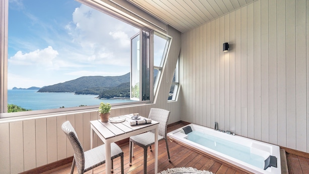 A balcony with a view of the sea, a table with chairs, and a bathtub. - Ruscello Pension (Geoje)
