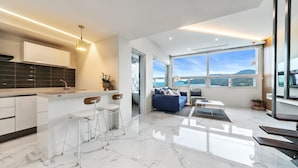 A modern kitchen with a marble countertop, bar stools, and a large window offering a view of the sea. - Ruscello Pension (Geoje)