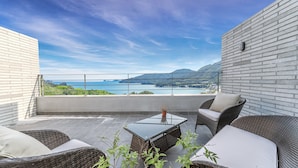 A balcony with wicker furniture, a small table, and a view of the sea and mountains. - Ruscello Pension (Geoje)