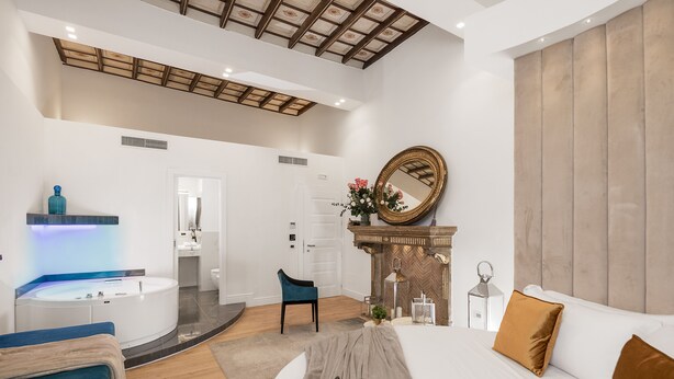 A modern hotel room with a large bed, a sitting area with a blue chair, a bathroom with a bathtub, and a fireplace. - Navona Style (Rome)