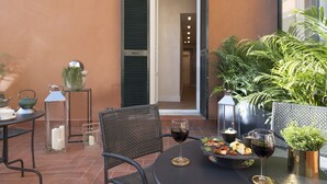 A patio with a round table, chairs, a wine glass, a tray with food, and potted plants. - Navona Style (Rome)