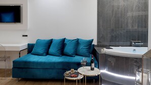 A modern living room with a teal sofa, a small round table with a bottle and glasses, and a large bathtub. - Navona Style (Rome)
