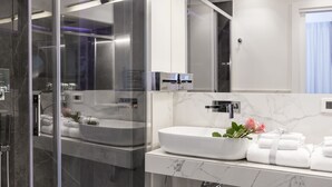 A modern bathroom with a glass-enclosed shower, a white marble sink, and neatly folded towels. - Navona Style (Rome)