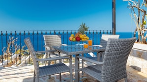 A wicker table and chairs set on a balcony with a fruit bowl and drinks, overlooking a clear blue sea. - Olive Resort (Petrovac)