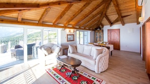 A spacious living area with a high wooden ceiling, a white sofa, a coffee table, and a view of the outdoors. - Olive Resort (Petrovac)