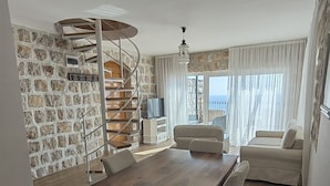 A dining area with a wooden table and wicker chairs, a spiral staircase, a sofa, and a view of the sea. - Olive Resort (Petrovac)