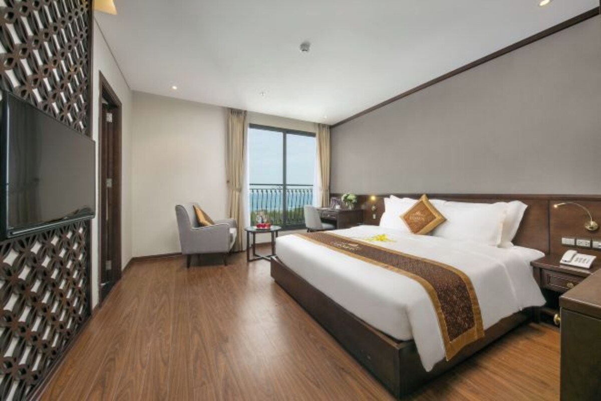 Habitación de hotel con una cama grande, un escritorio, una silla, un televisor y un balcón con vistas.