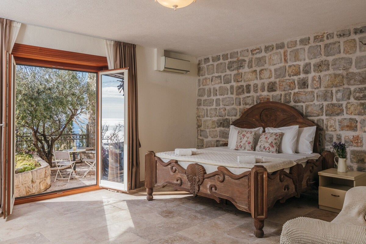 A bedroom with a stone wall, a wooden bed, a balcony with a view, and a ceiling light.