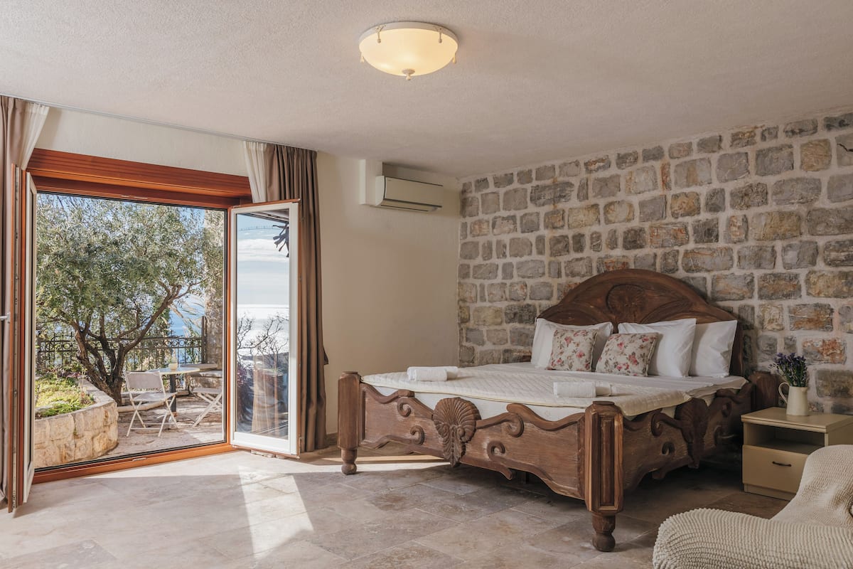 A bedroom with a stone wall, a wooden bed, and a balcony with outdoor furniture.