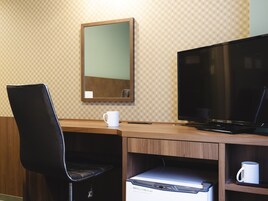 Habitación de hotel con un escritorio de madera, una silla negra, un televisor, una taza blanca y un pequeño electrodoméstico.