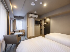 Habitación de hotel con dos camas, un escritorio, una silla, un televisor y aire acondicionado.