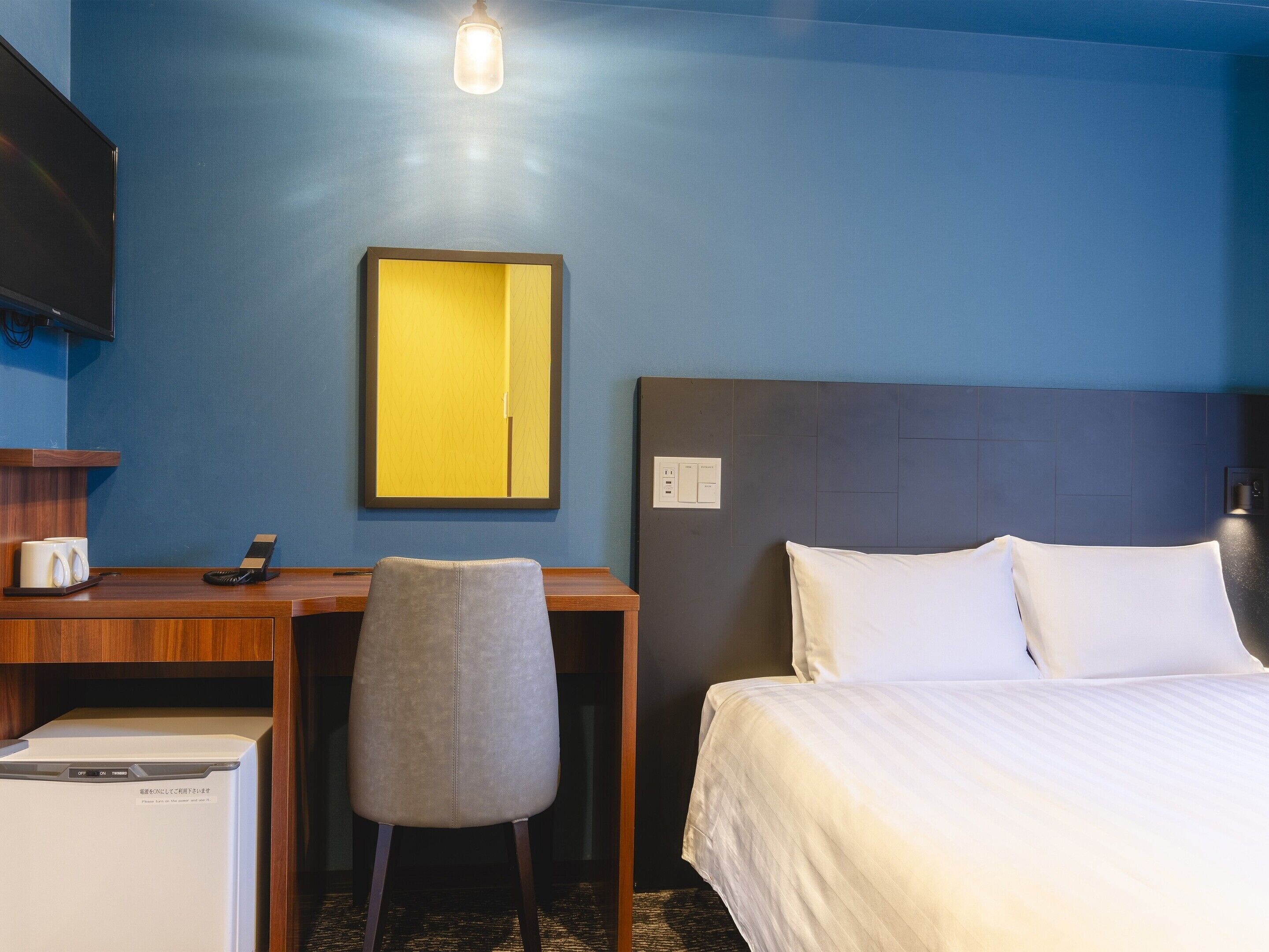 A hotel room with a bed, desk, chair, and a mirror.