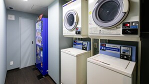 A laundry facility with two front-loading washing machines and a blue vending machine. - KOKO HOTEL Shimbashi Onarimon (Tokyo)