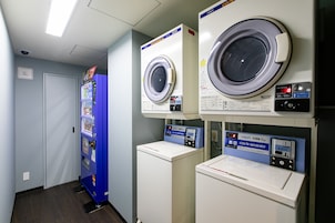 Un cuarto de lavandería con dos lavadoras de carga frontal y una máquina expendedora azul.