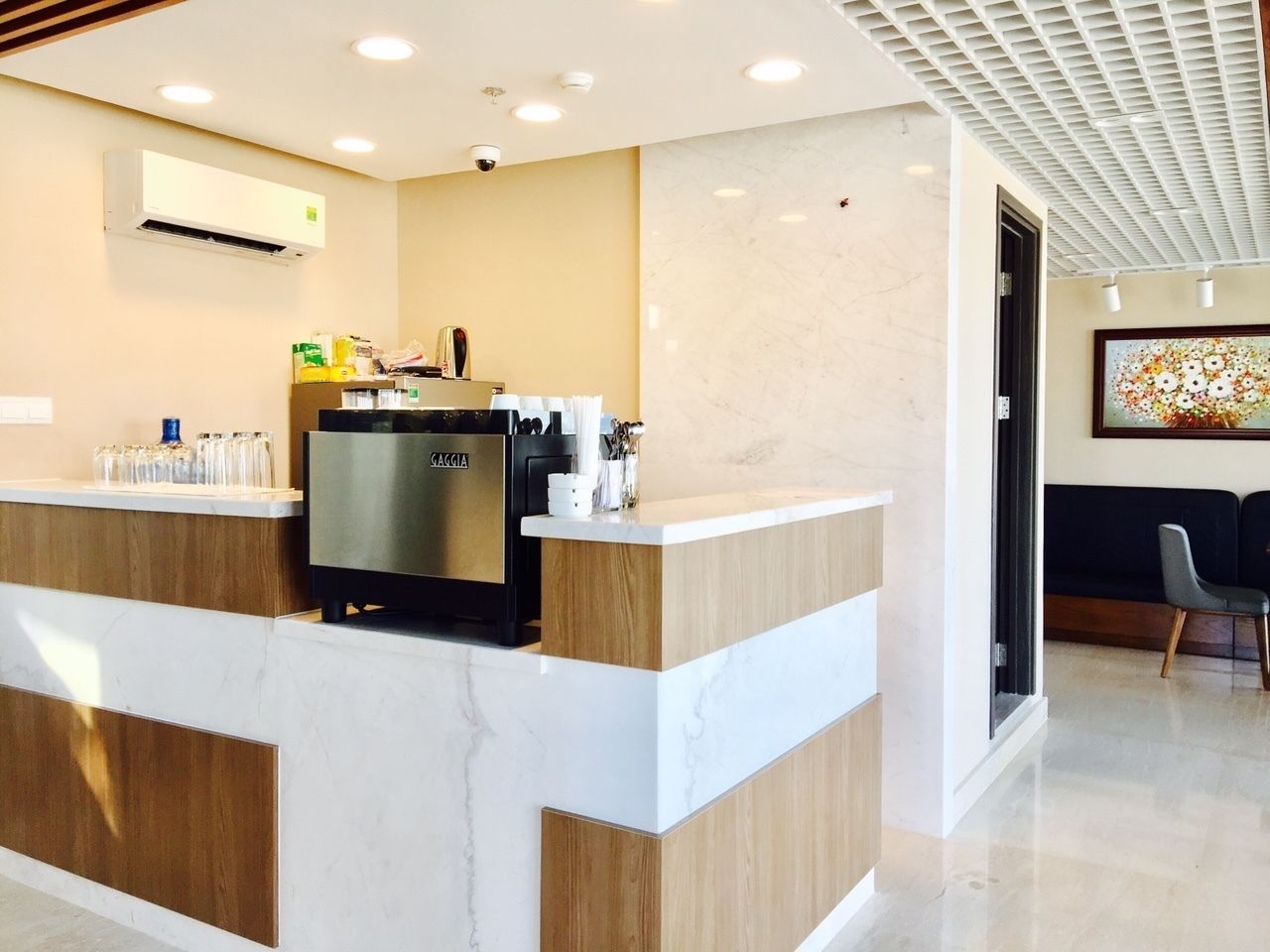 A modern reception area with a marble counter, a coffee machine, and a seating area with a black couch and a chair.