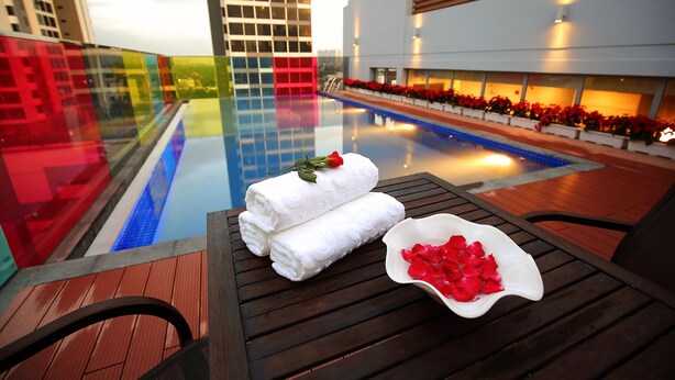 Un espace aménagé au bord de la piscine, avec une table en bois, deux serviettes enroulées et un bol rempli de pétales de rose.