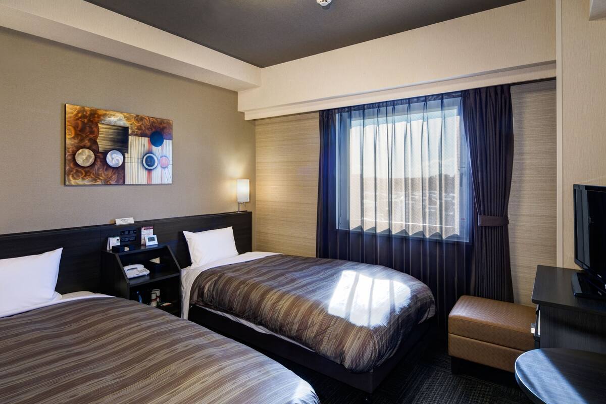Une chambre d’hôtel avec deux lits, un bureau, une chaise, une télévision et une fenêtre avec des rideaux.