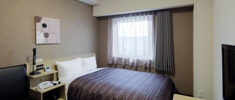 Habitación de hotel con cama, escritorio, silla, televisor y ventana con cortinas.