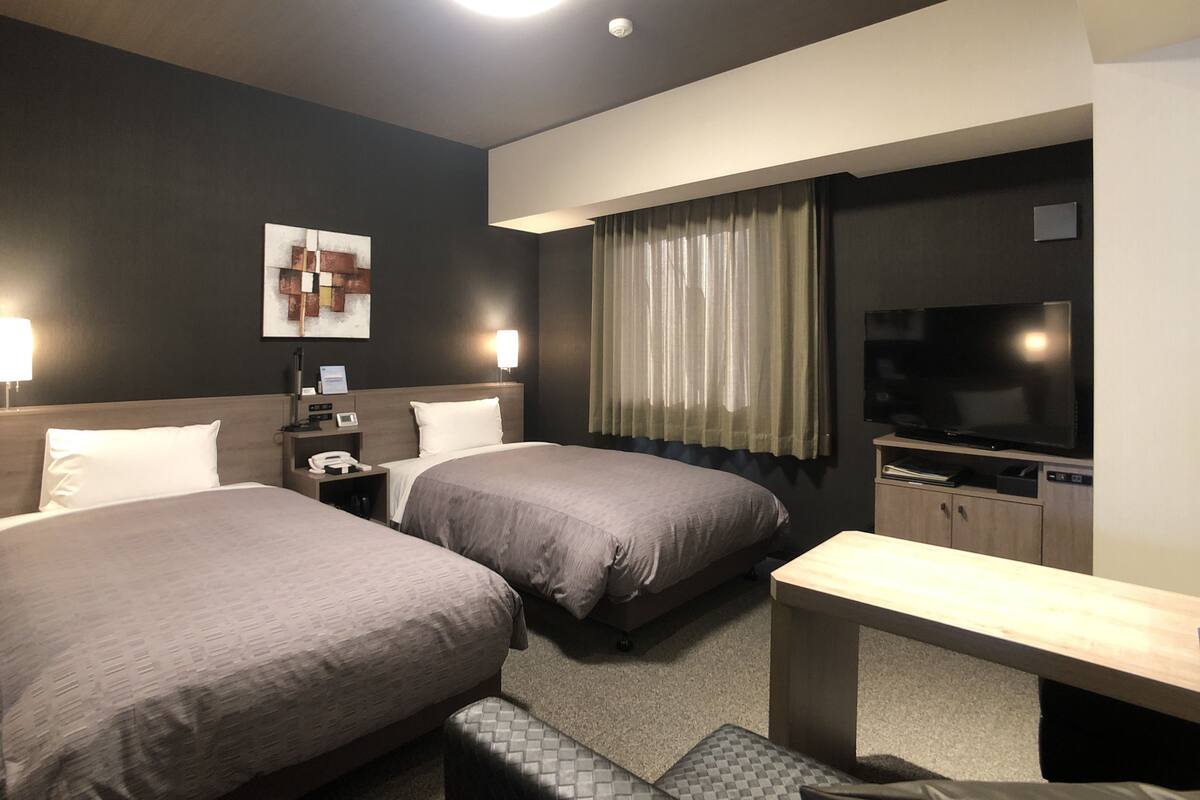 Une chambre d’hôtel avec deux lits, une télévision, un bureau et une lampe.