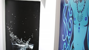 Um quarto com uma grande pintura abstrata em preto e branco de um respingo de água na parede, piso ladrilhado e um mural colorido na parede vizinha.