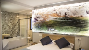 Quarto de hotel moderno com uma cama grande, chuveiro e uma obra de arte na parede retratando uma cena natural.