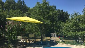 A swimming pool with a yellow umbrella, surrounded by greenery and outdoor furniture. - Le Peyrail (Les Lèves-et-Thoumeyragues)